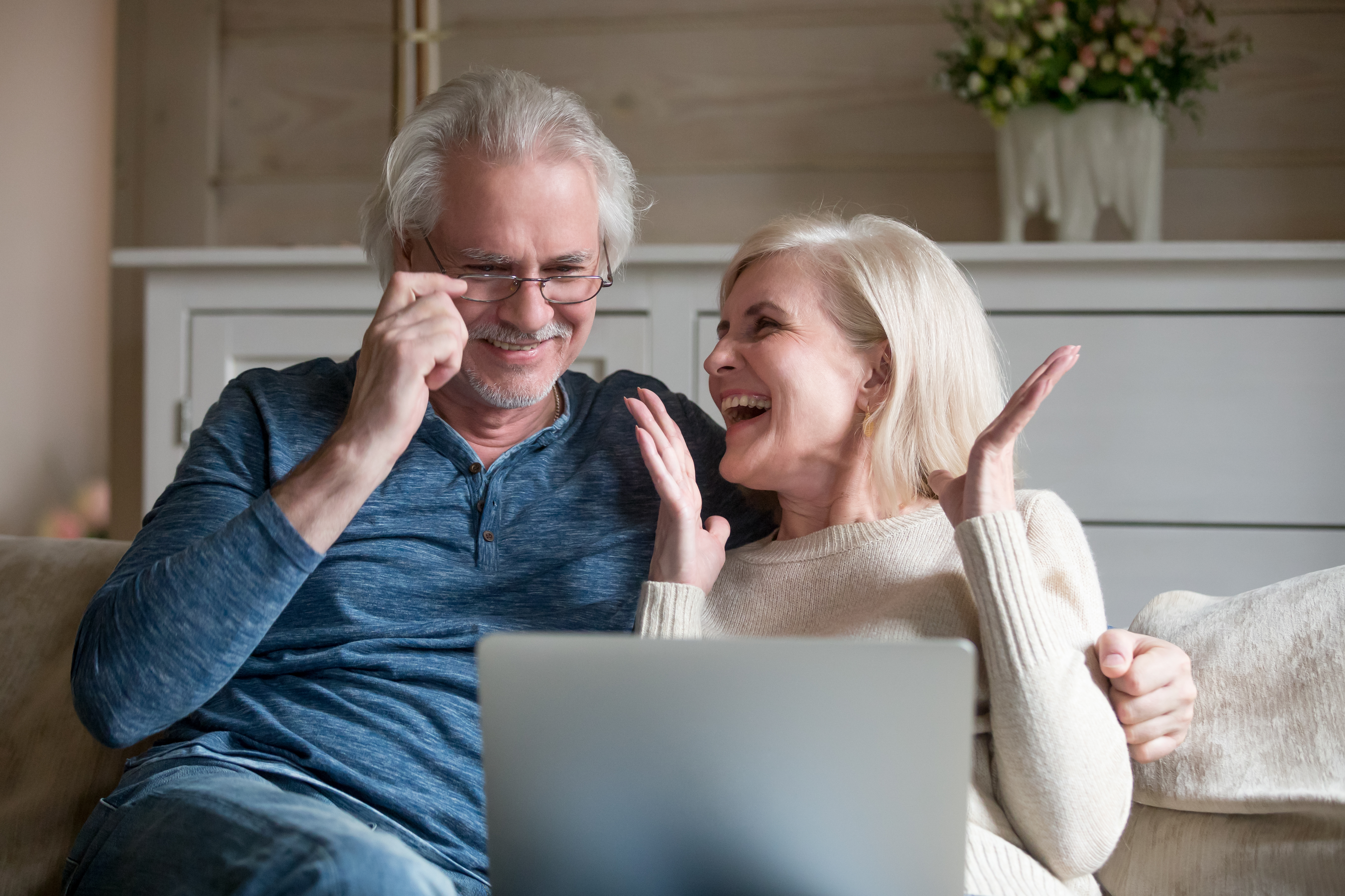  Older couple sitting on couch while happily looking at laptop.