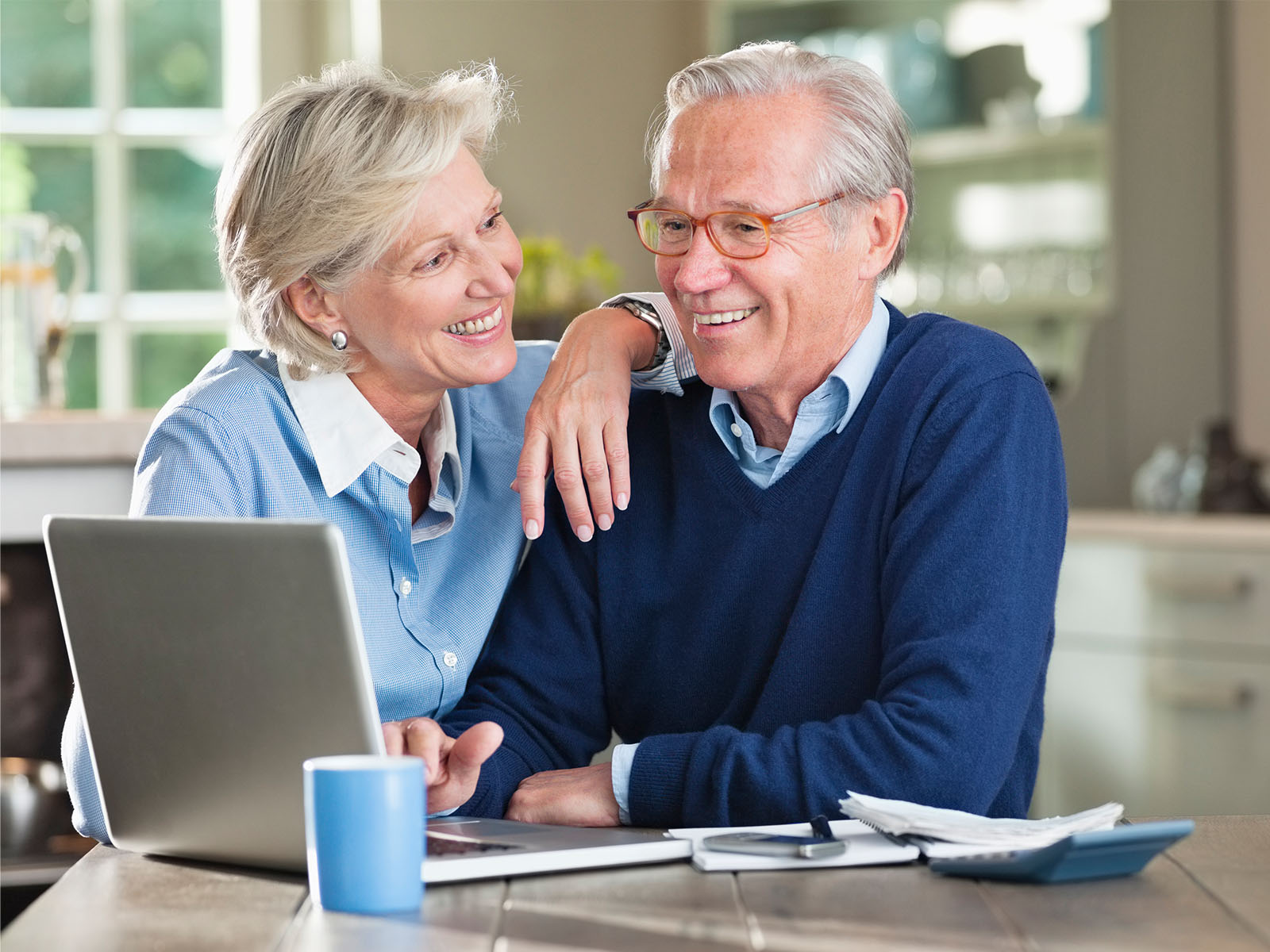 Senior couple smiling with laptop on kitchen table.
