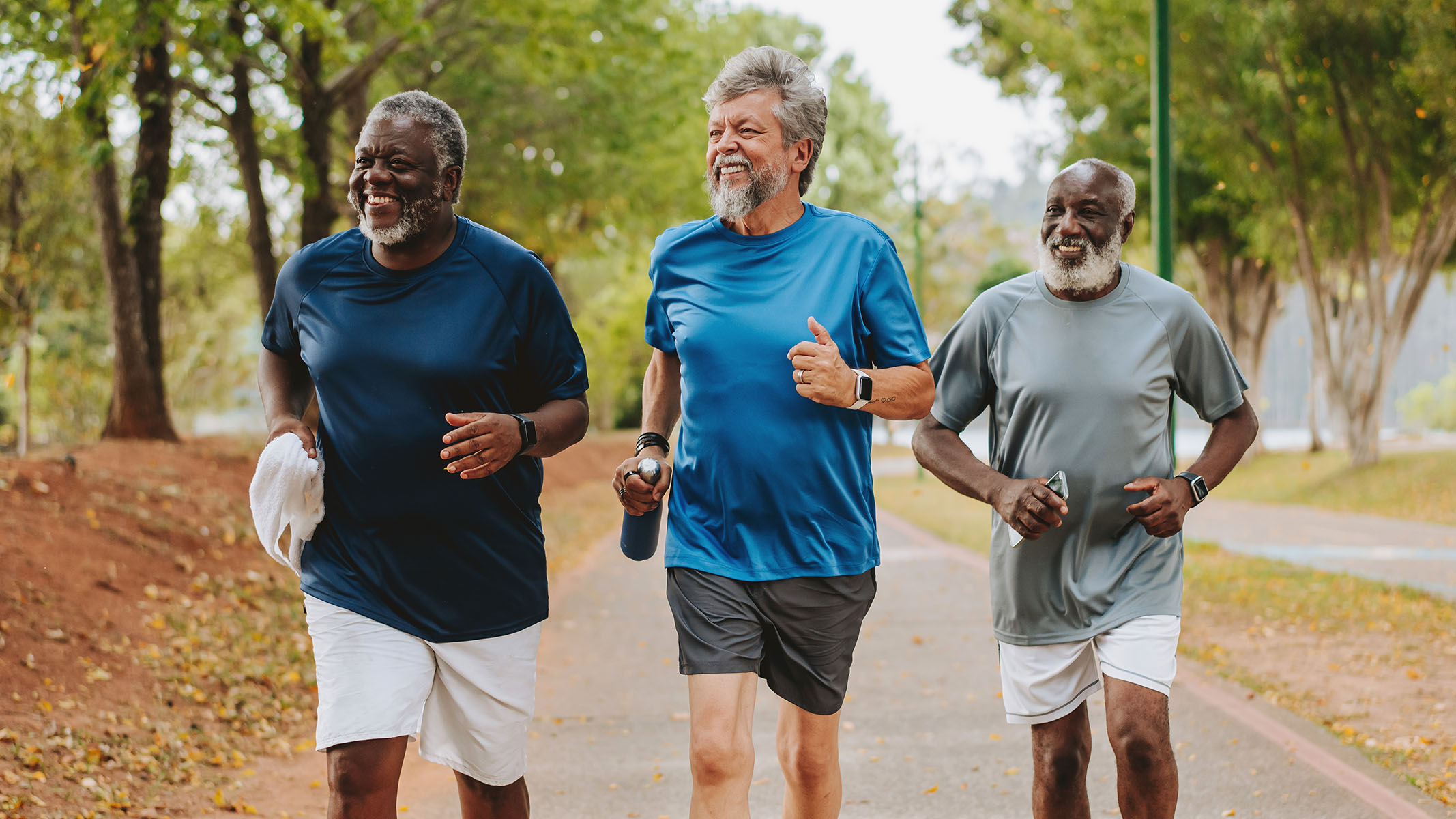 Three senior men power walking outside.