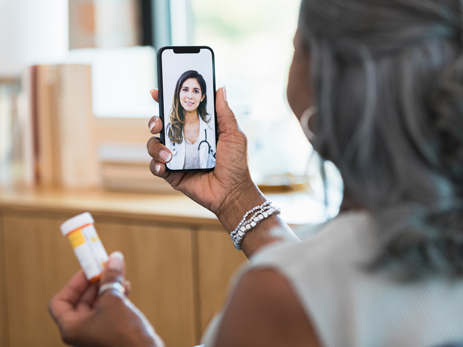 Woman video chatting  with a doctor holding a prescription bottle.