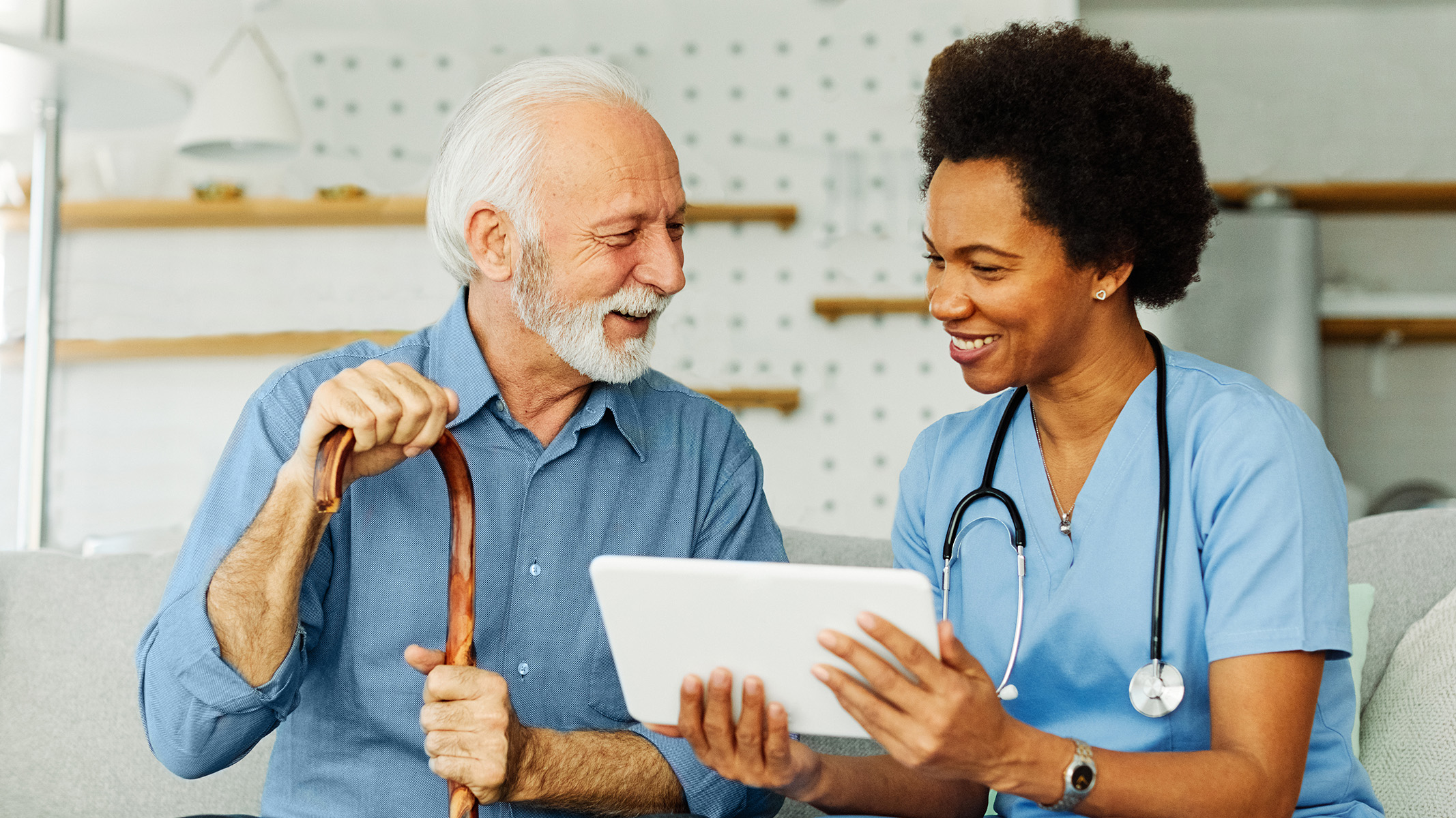  Nurse with stethoscope and tablet smiling with senior man using a walking stick.
