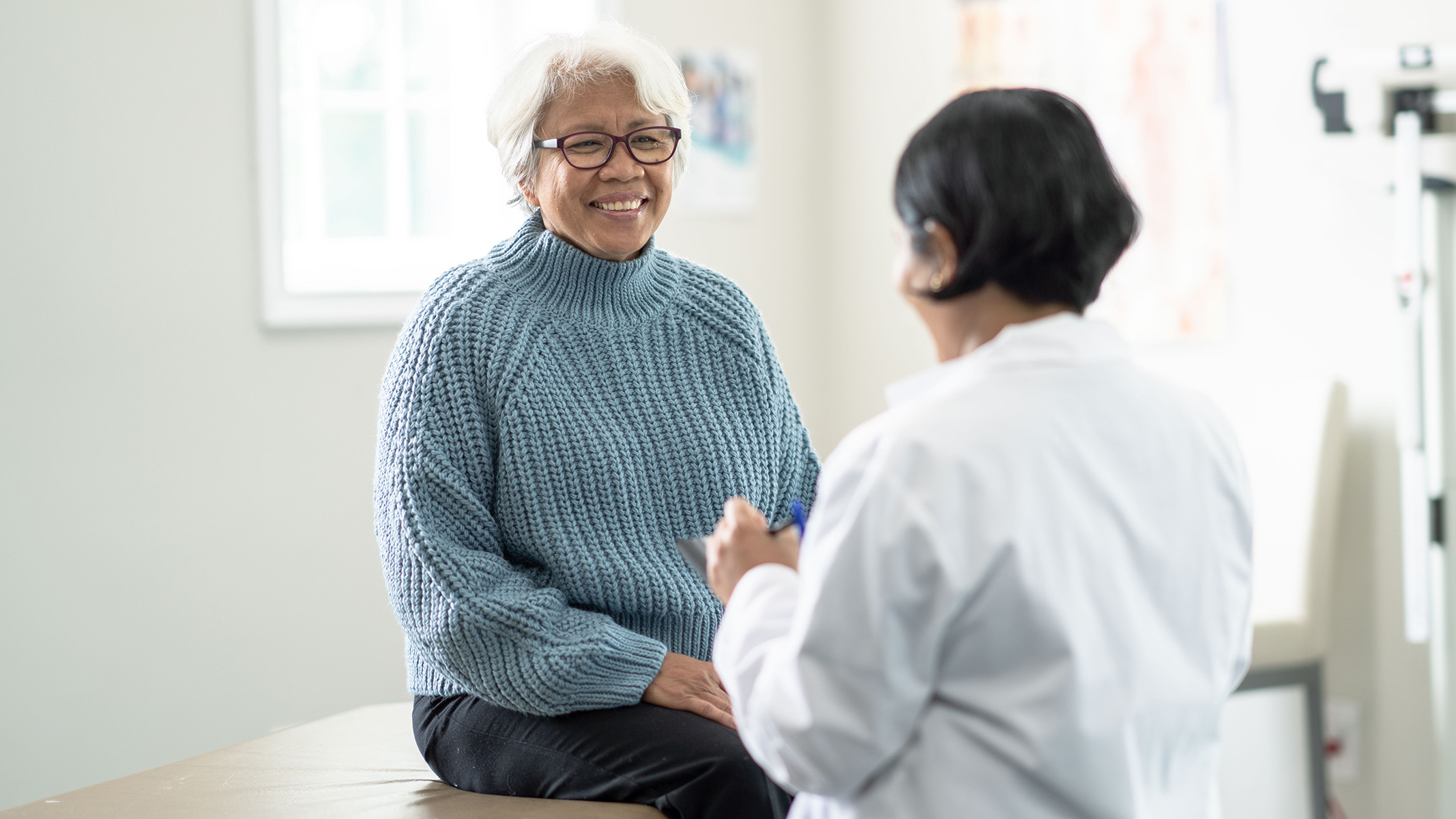  Senior woman sitting on an examination table talking to a doctor.
