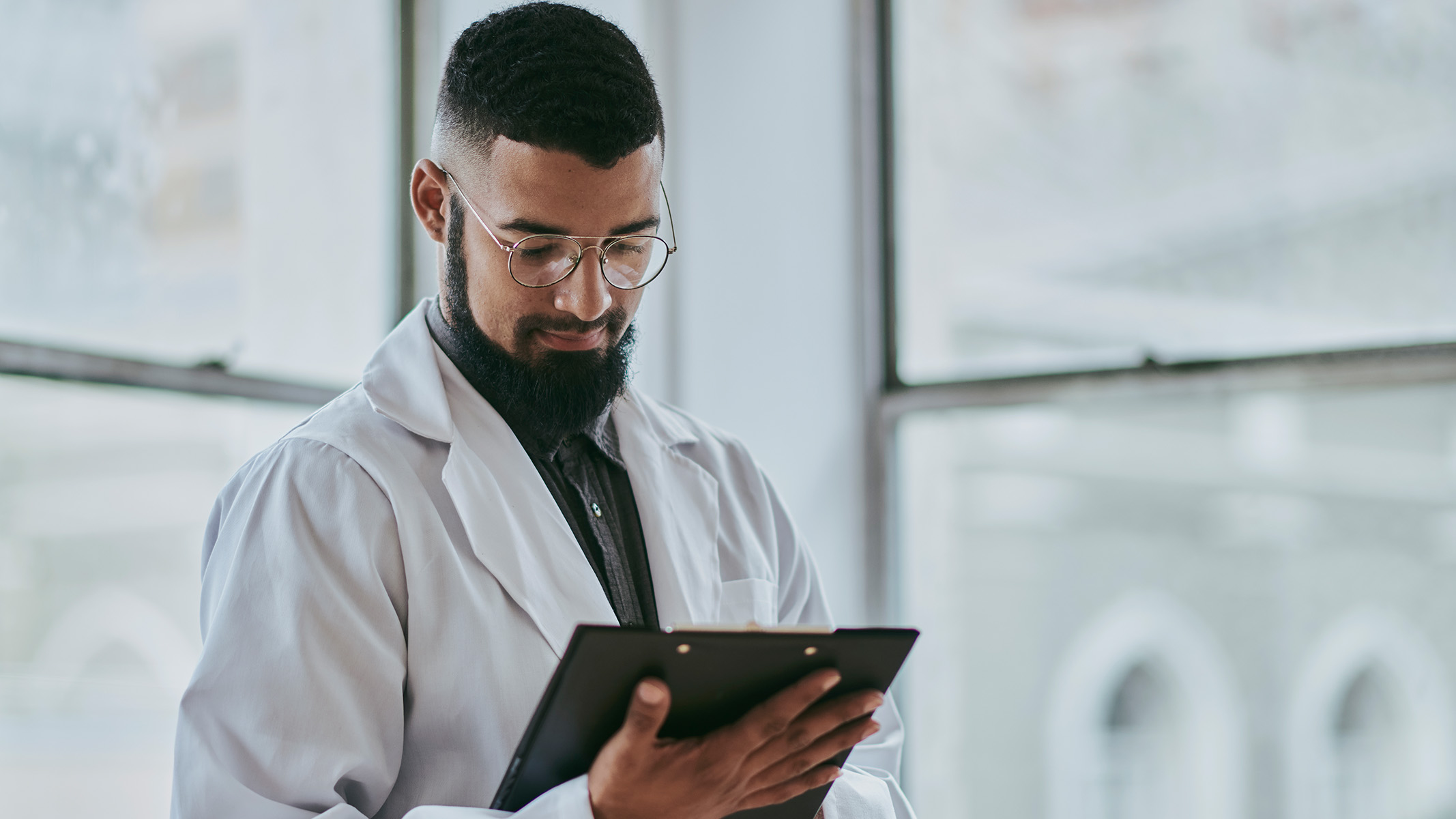 A young male doctor stands while looking down at a medical document.