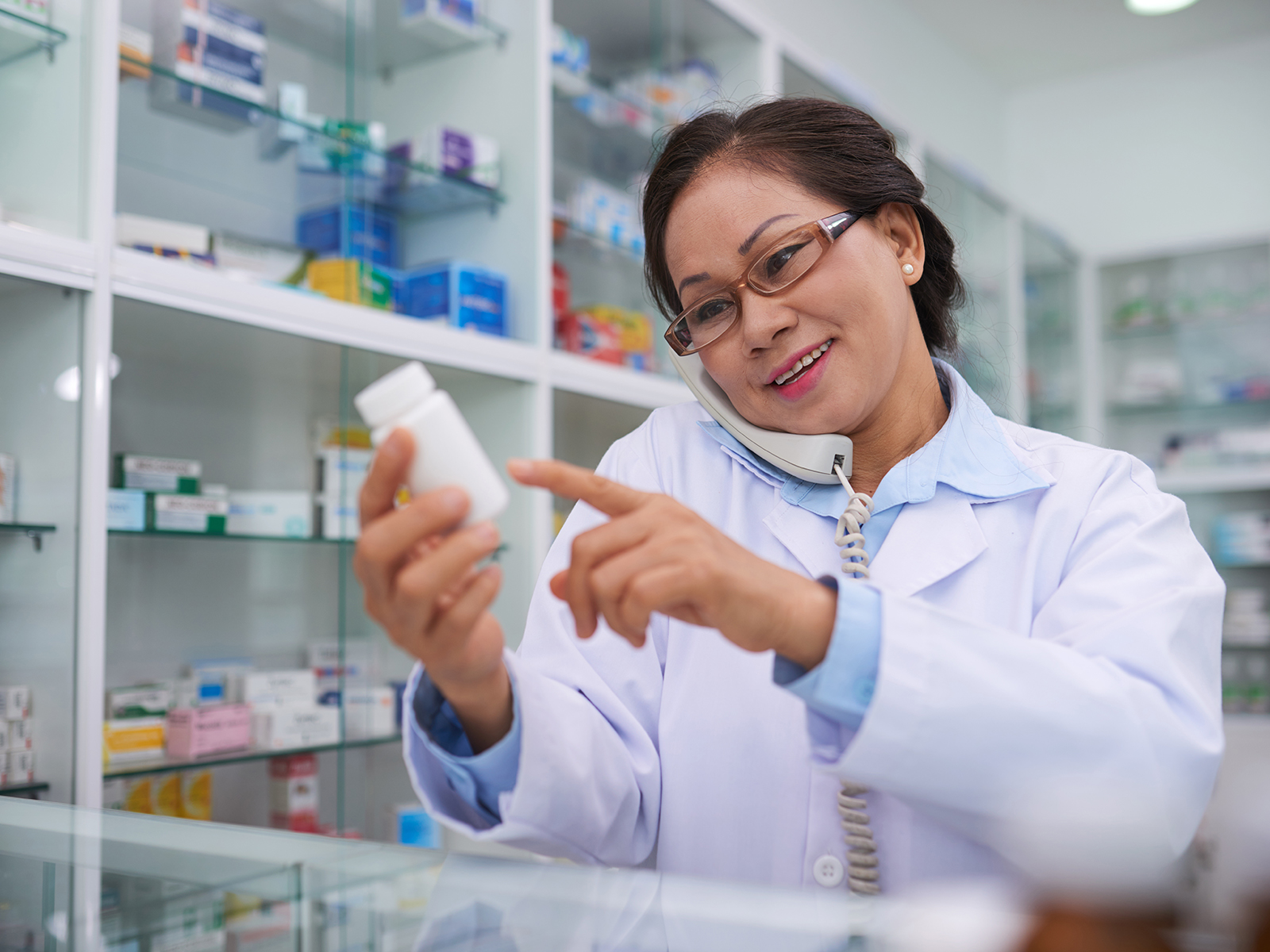 Pharmacist reading medication label while on the phone.