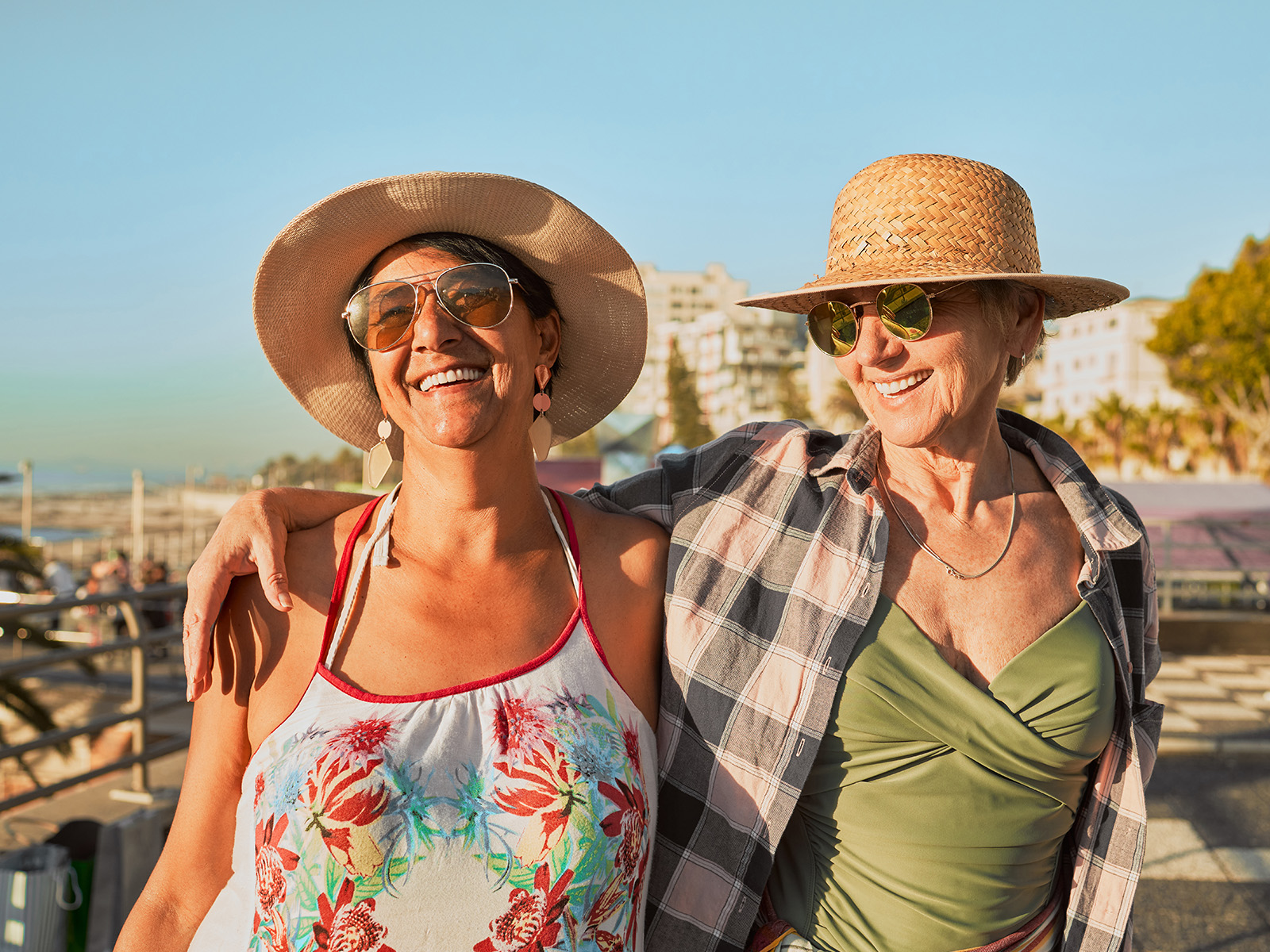Two senior women take a walk on a pier, smiling and enjoying a sunny day.