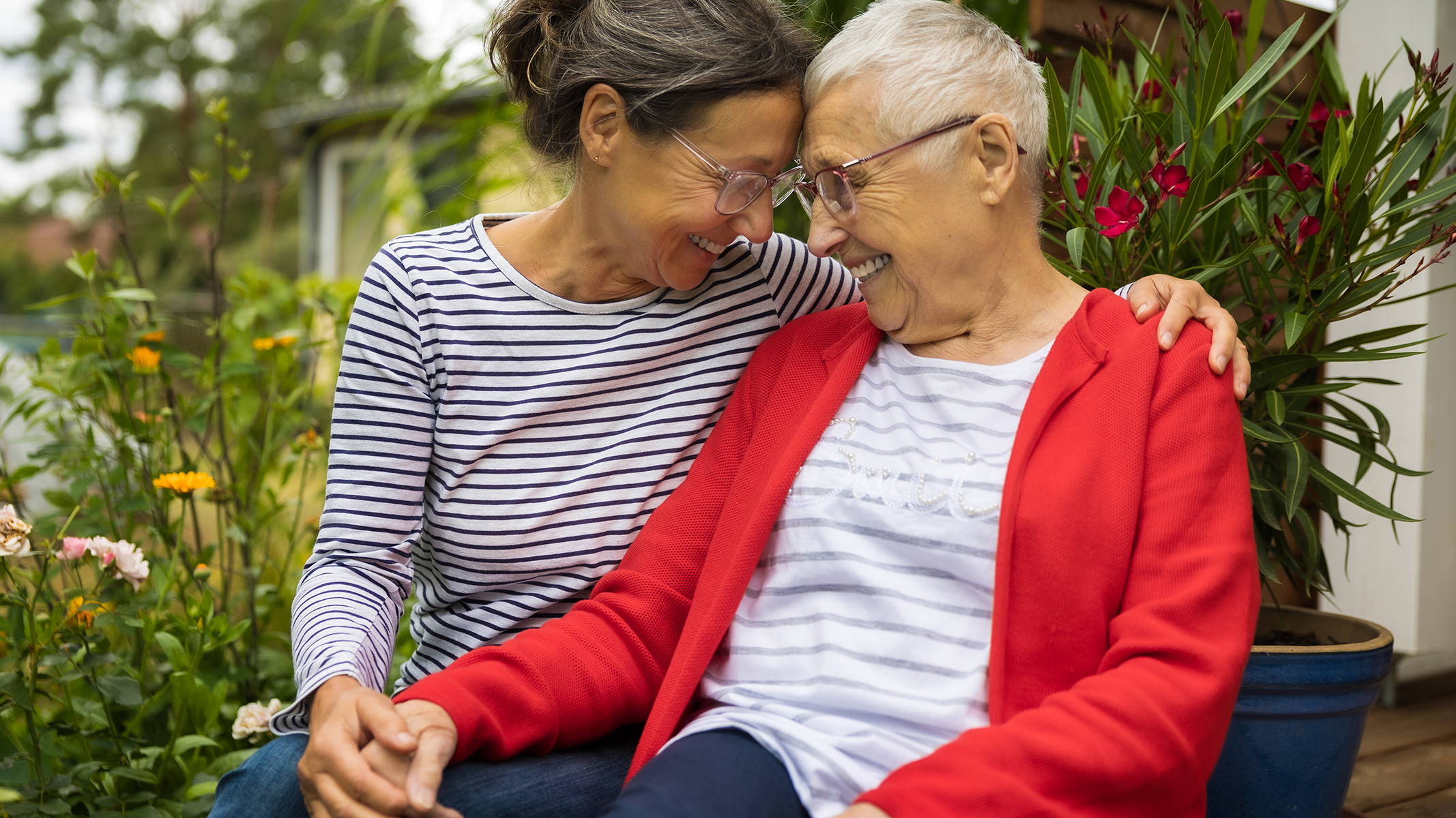 A senior woman and her caregiver sitting next to each other in a garden