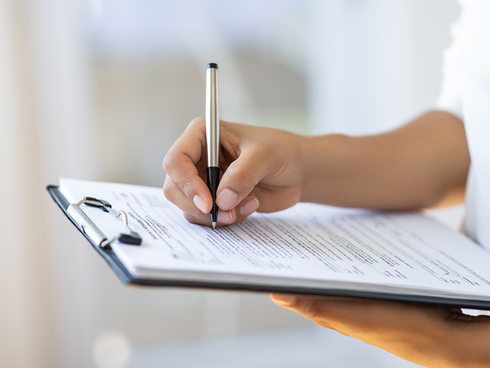 The hand of a person filling out a form attached to a clipboard