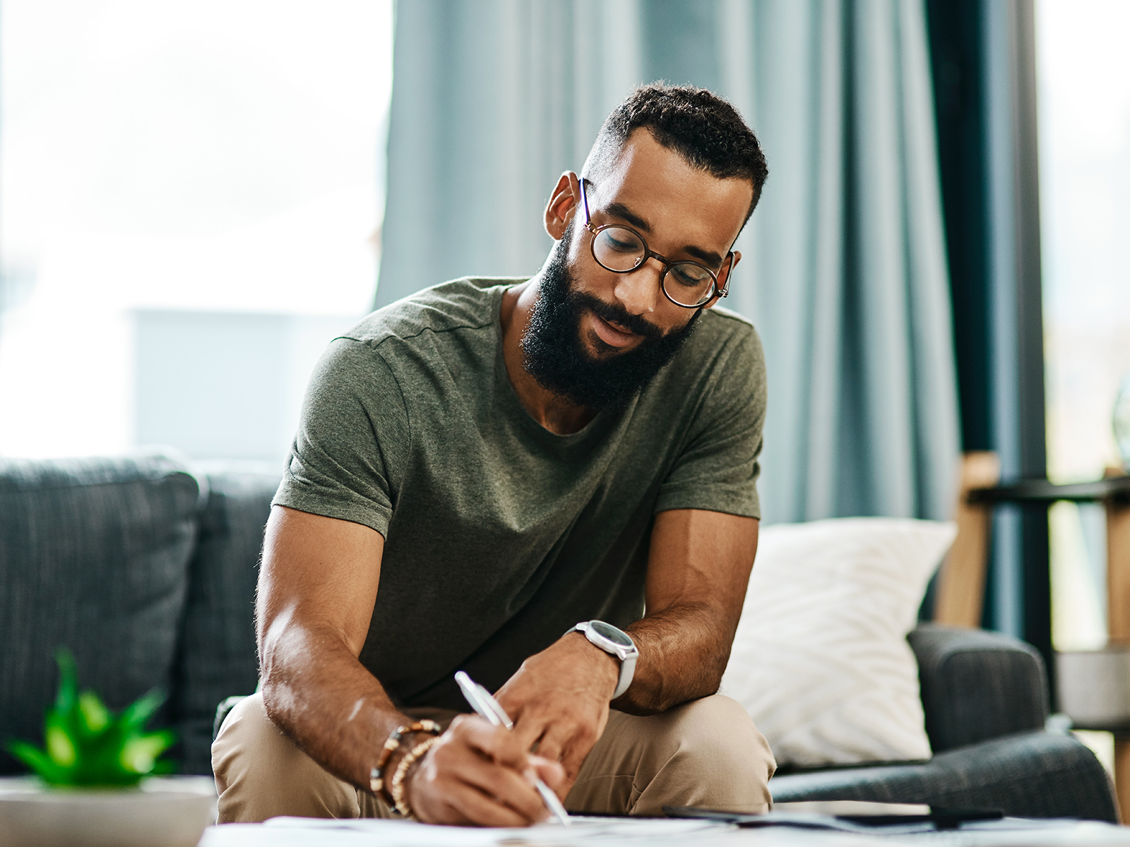 A man sitting on the couch filling out paperwork at a coffee table