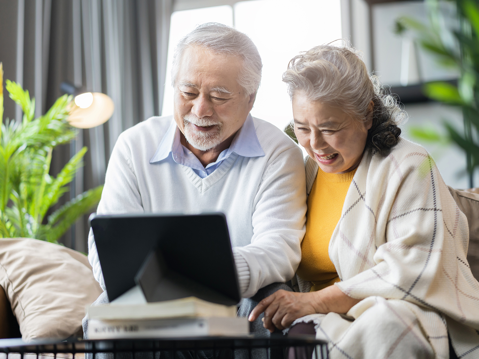 Personas mayores sentadas en el sofá y sonriendo frente a una laptop abierta.