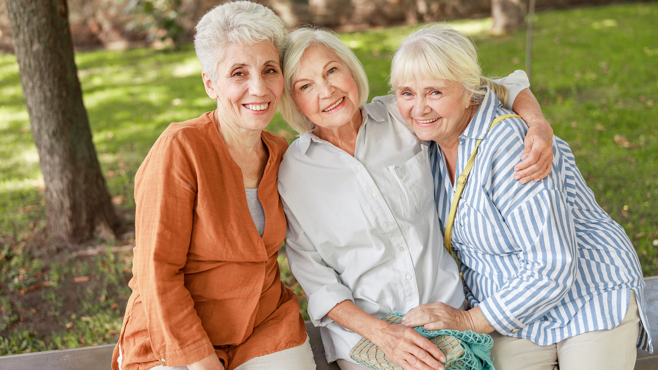 Grupo de 3 mujeres mayores sonriendo en un banco de la plaza