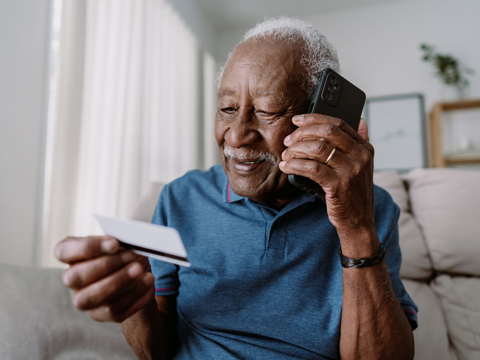 Hombre mayor sonriendo sentado en el sofá mientras habla por teléfono