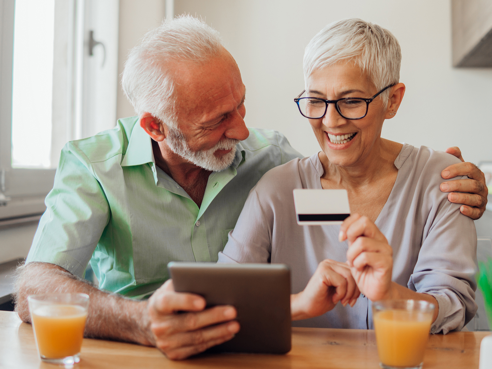 Senior man and woman holding a card while using a tablet.