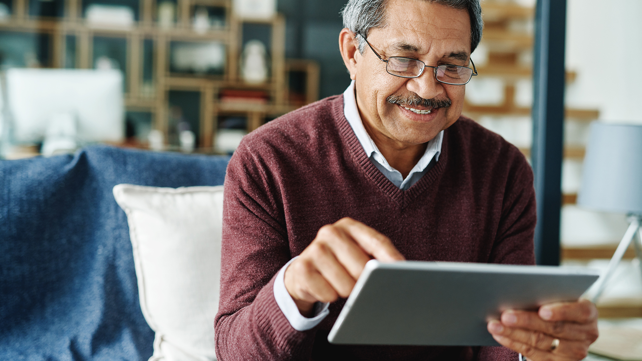 Senior man smiling while using tablet and sitting on the couch.