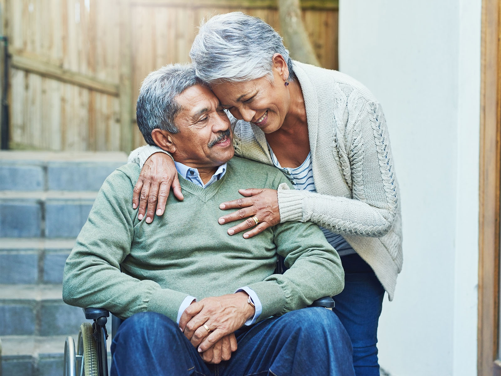 Elderly man in wheelchair being hugged by his wife.