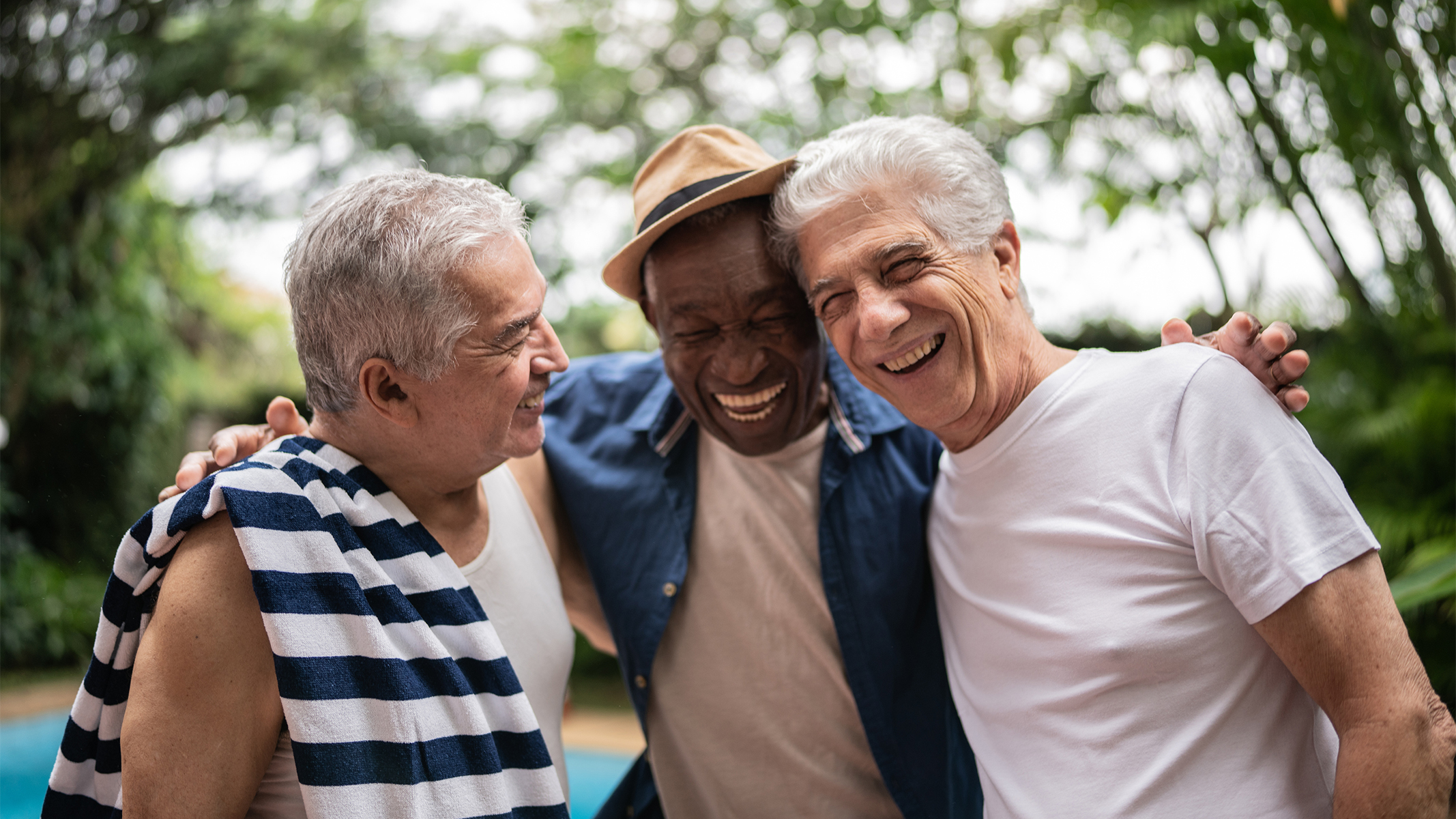 Tres hombres mayores sonriendo junto a la piscina.