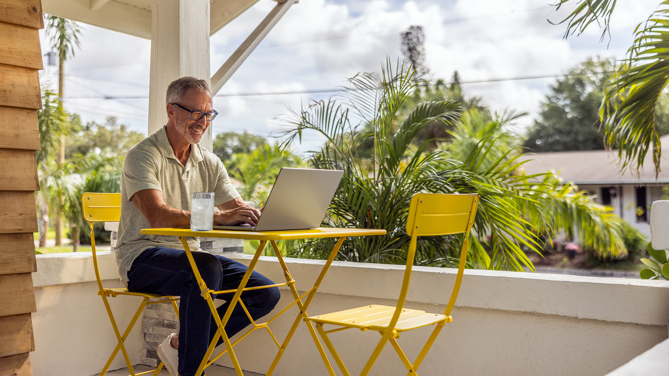 Una persona mayor sentada al aire libre en un entorno tropical utilizando su computador portátil.