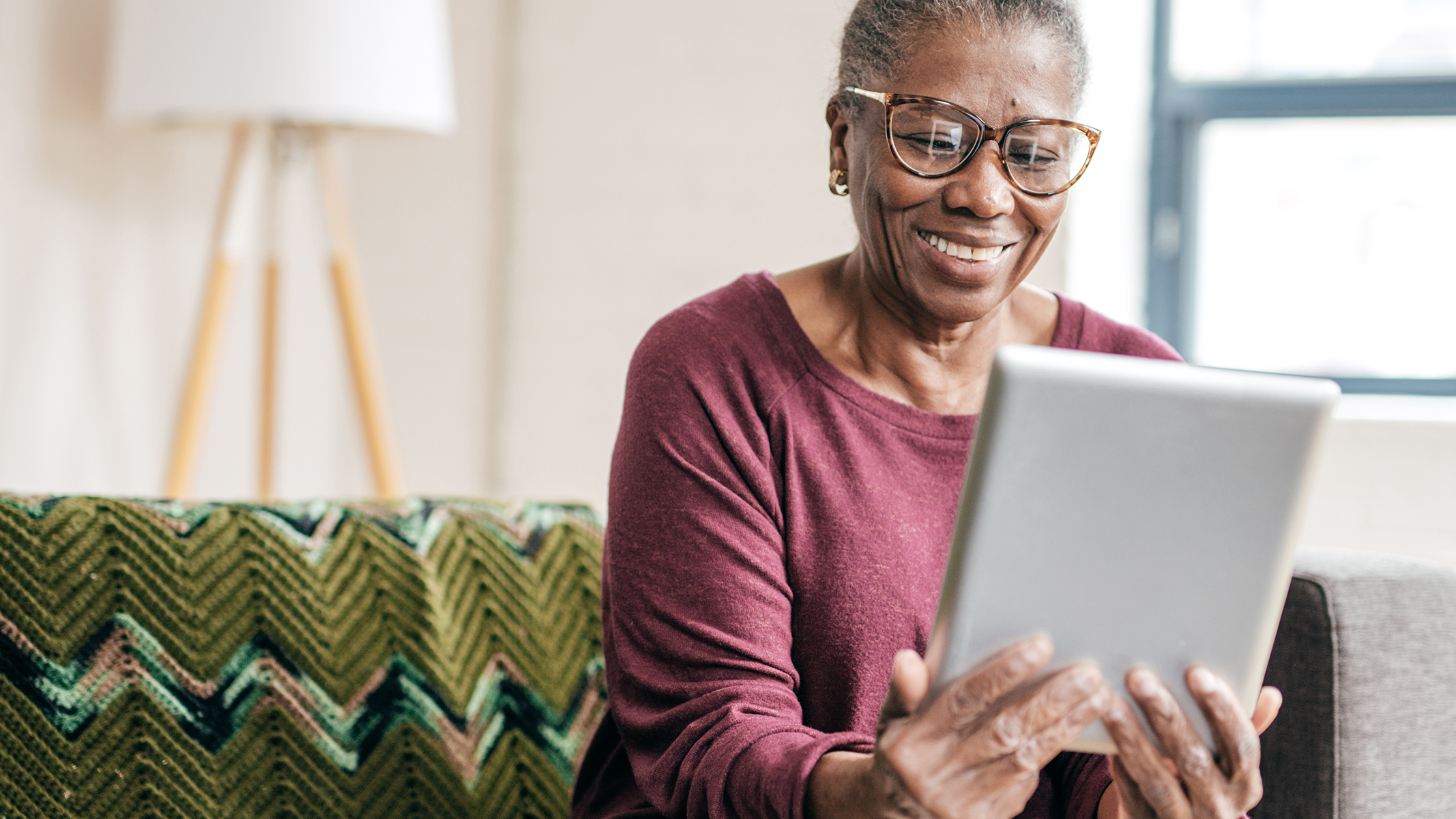 Senior woman smiling while sitting and holding a tablet.