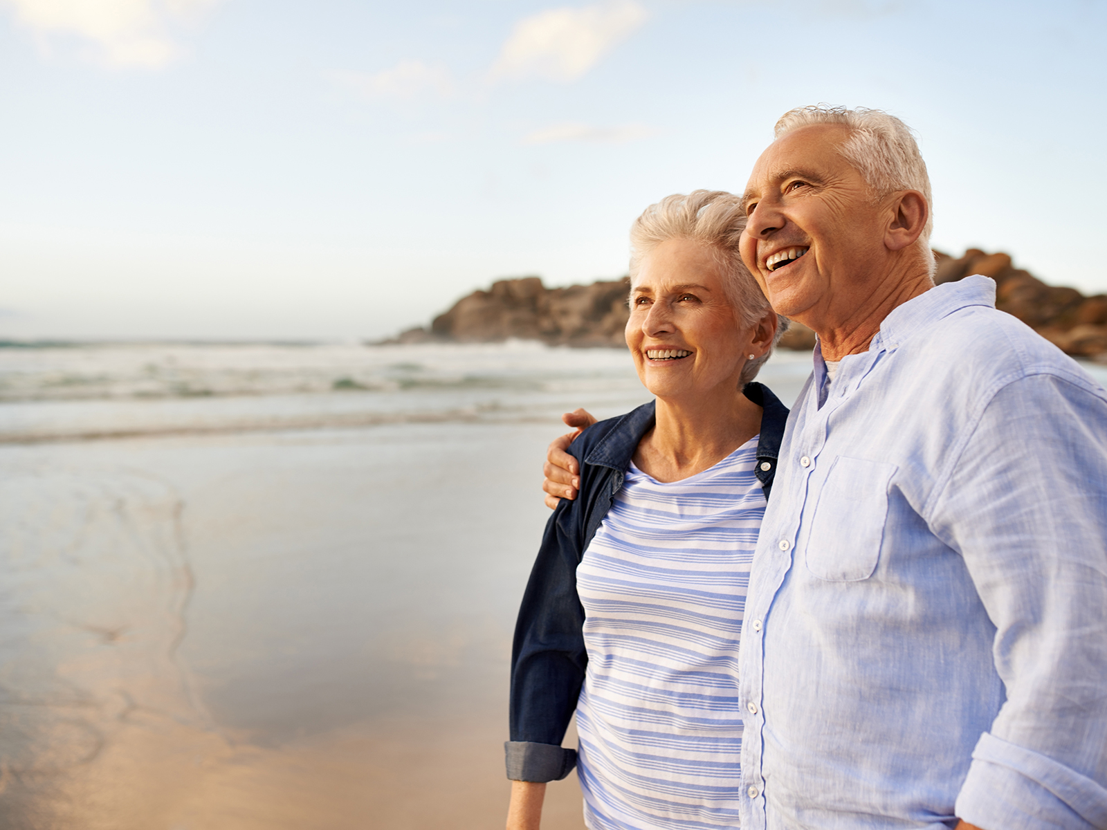 Pareja de personas mayores sonriendo en la orilla de la playa.